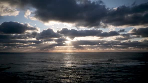 The sun just above the passing clouds shining rays of light down to the Pacific Ocean. A blue and or