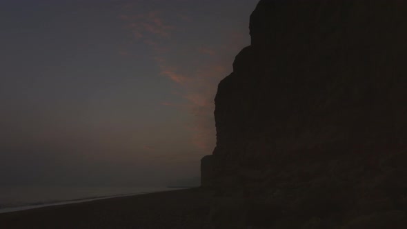 Timelapse - sun sets next to large towering cliffs by the sea