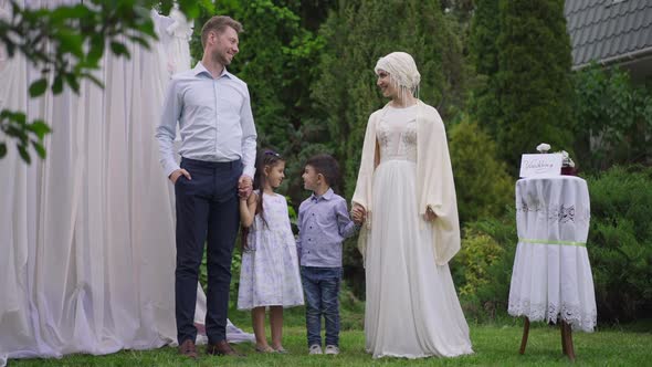 Wide Shot Portrait of Happy Interracial Newlyweds Posing with Children at Wedding Altar in Spring