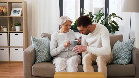 Adult Son Bringing Coffee To Senior Mother at Home