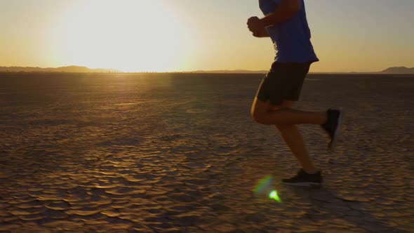 Athletic man working out with battle ropes on a dry lake at sunset