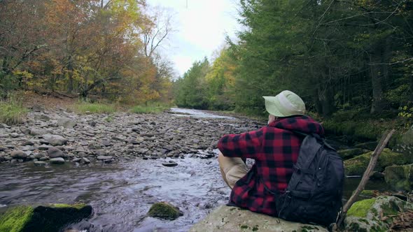 An older hiker resting by a creek in a scenic forest in the mountains.