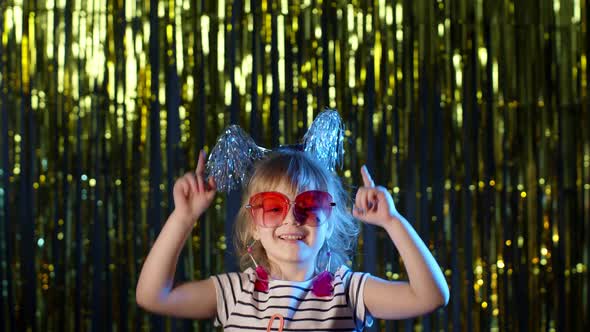 Stylish Teenager Kid Girl Standing on Backlit Blue Neon Lights and Points at Blank Space Agree Sign