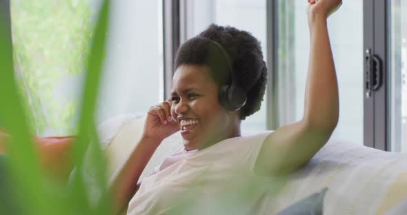 Happy african american woman wearing headphones sitting on sofa