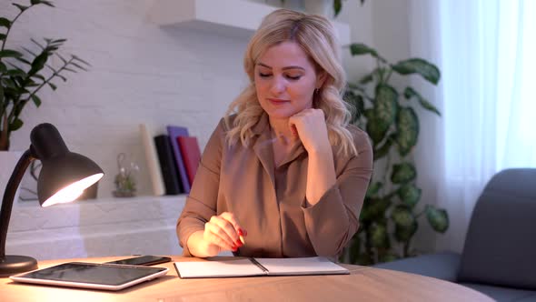 Smiling Attractive Woman Thinking About Something Then Writing Something in Notebook While Sitting