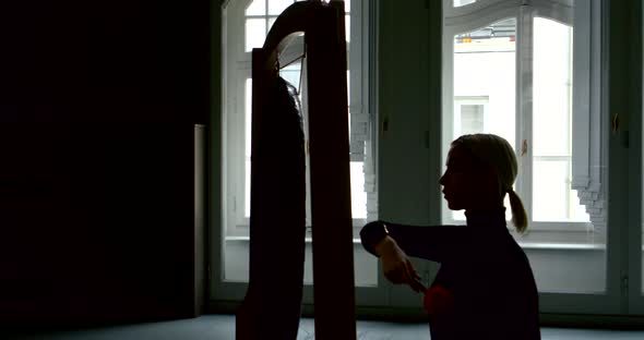 A Young Slender Blonde Girl Is in a Large Studio with Large Windows, She Sits at the Gong and Beats