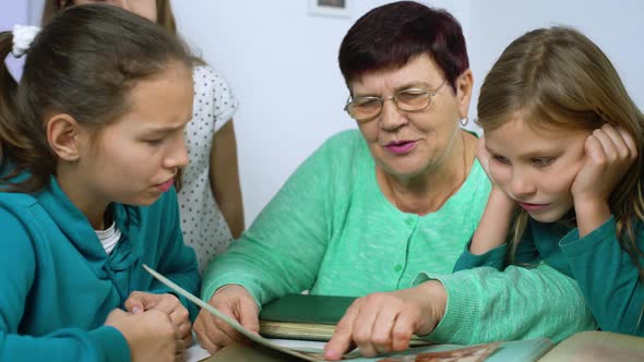 Grandmother Showing Old Photo Album to Her Four Granddaughters