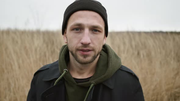 Young Guy Standing In The Field With Dry Grass. Serious Guy With Sadness In His Eyes. Concept Of