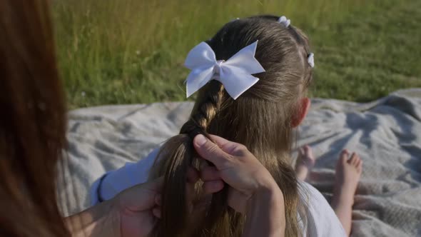 Closeup of Mother's Hands Braiding the Daughter's Braid in Nature