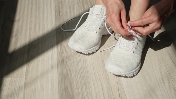 Young Girl Tying Her Shoelaces on Sporty White Sneakers for a Walk or Jogging Outdoors Closeup