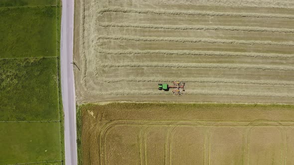 Harvesting tractor with its twin rotor rake trailer filmed from above working at a field, collecting