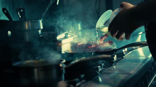 Professional chef pours oil into a flaming pan to cook meat.