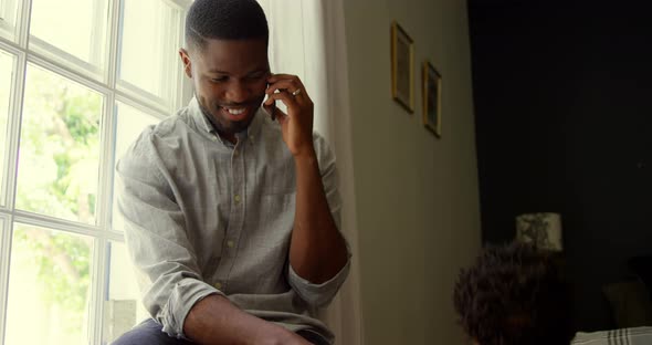 Front view of young black father talking on mobile phone with baby in a comfortable home 4k