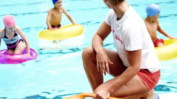 Female lifeguard looking at students playing in the pool