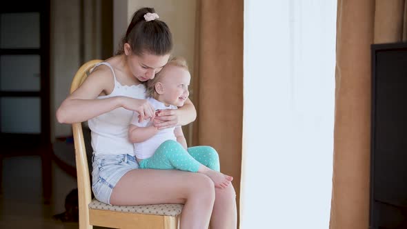 A young mother takes care of the nails of a little restless daughter