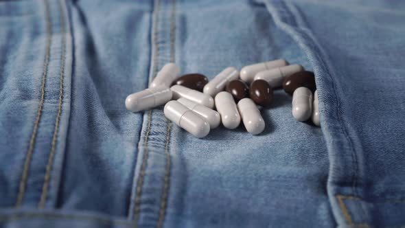 A handful of medical capsules on blue jeans. White and brown. 