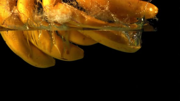 Super Slow Motion on a Black Background Bananas Fall Under the Water with Air Bubbles