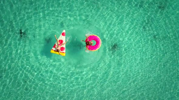 Close aerial view of two young girls swimming and playing in sea with inflatables.