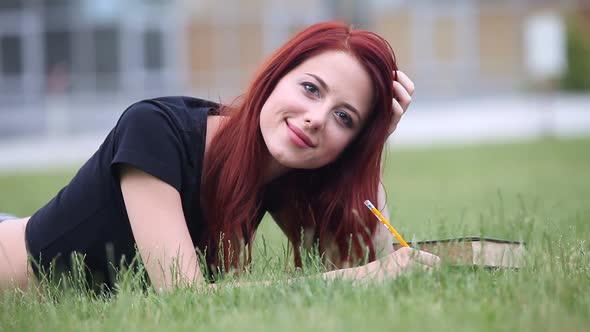 redhead girl with notebook and books lying on green grass