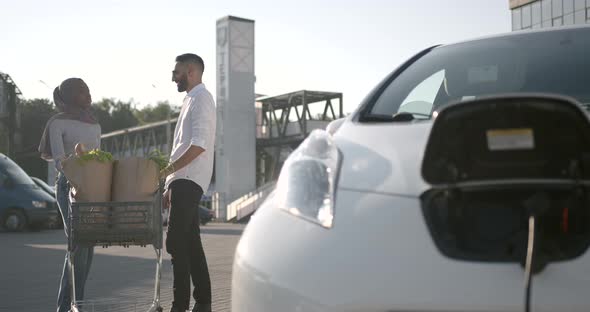 Multi Ethnic Couple Charge Elctric Car After Shopping