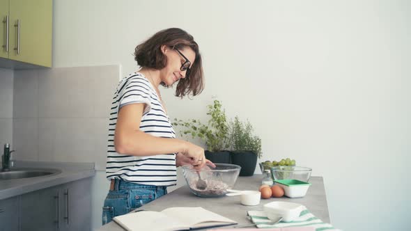 Young Cheerful Woman in Glasses Cooking at a Bright Kitchen and Dancing