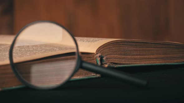 Magnifying Glass Lies on the Background of an Old Book and the Girl Puts a Pen