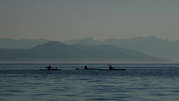 Silhouettes of Tourists on Kayaks Moving on Mountain Range Background