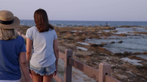 Mother and daughter walking down the wooden pier by the sea at sunset