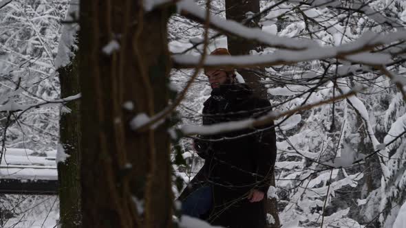 Young east european men walks through the snowy woods in winter clothes with his black camera.