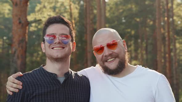 Portrait of Two Affectionate Gay Men in Love Wearing Sunglasses of Heart Shape Smiling To Camera