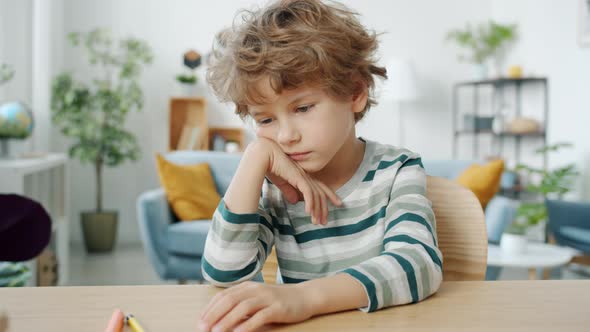 Bored Child Sitting at Table at Home Feeling Unhappy and Lonely