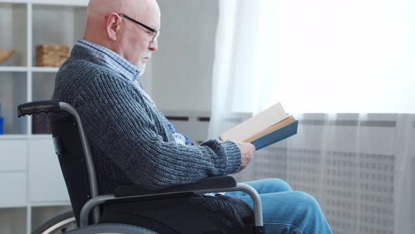 Disabled old man is sitting in a wheelchair at home alone. A handicapped person.