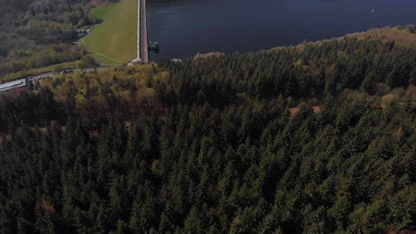 Drone shot travelling backwards out from a forest revealing the Lady Bower Reservoir in the far dist