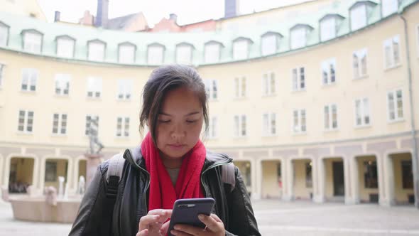 Asian woman wearing winter outfits standing and using smartphone in front of yellow building