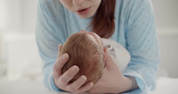 Pretty Woman Holding and Kissing Newborn Baby in Her Arms