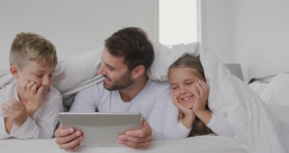 Father and children using digital tablet under blanket on bed at home 4k