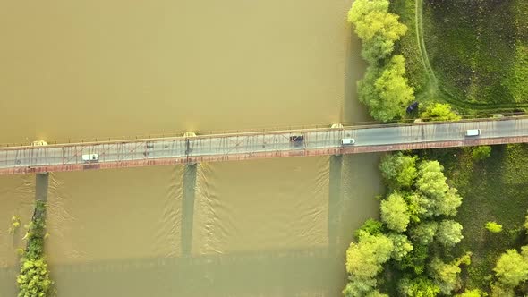 Aerial view of a narrow bridge over muddy wide river in green rural area.