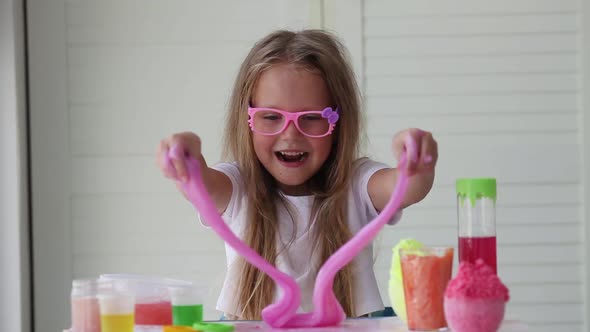 Little girl stretching pink slime to the sides. Kids hands playing slime toy