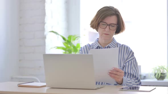 Senior Woman Reading Reports While Sitting in Office