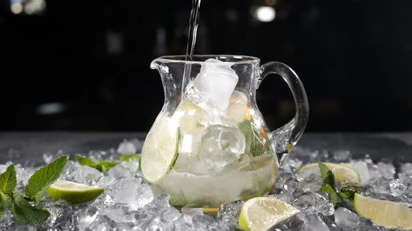 Sparkling Soda Water Being Poured Into Glass Jar Filled with Sliced Lime Mint Leaves and Ice Summer