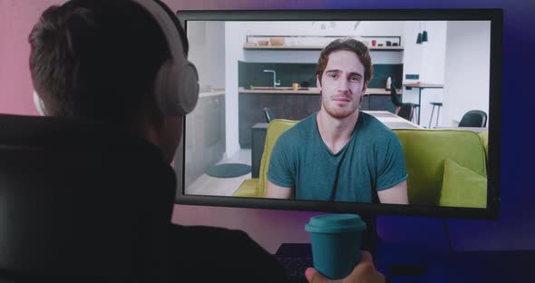 Rear View of a Young Man with Headphones Watching a Video Blog Indoors