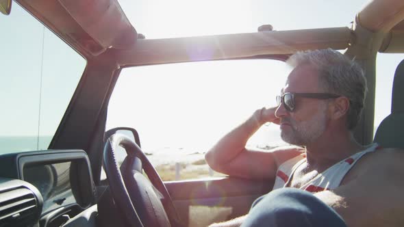 Thoughtful caucasian man in sunglasses sitting in car on sunny day by the sea