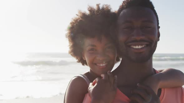 Portrait of smiling african american couple embracing on sunny beach