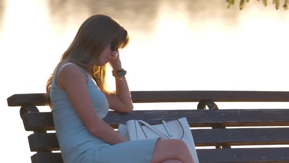 Lonely Sad Woman Sitting Alone on Lake Shore Bench on Warm Summer Evening