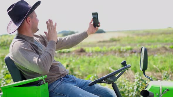 A Farmer Uses a Smartphone in a Field Near His Tractor