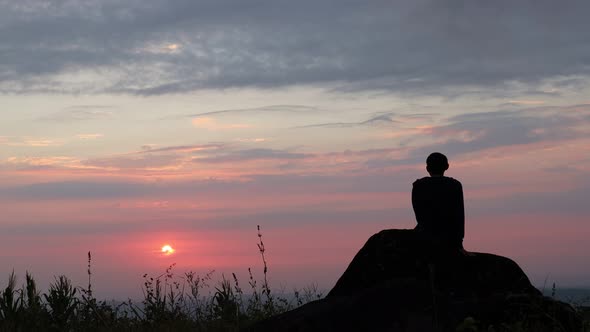 a man sits in a silhouette watching a beautiful sunrise