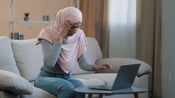 Young Muslim Woman in Pink Hijab Sitting on Sofa Working Using Laptop Having Headache Migraine Sad