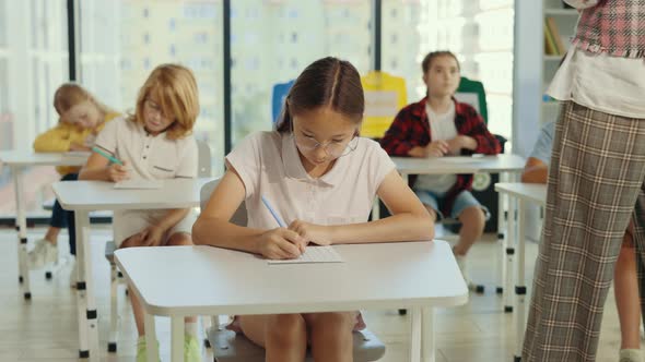 Beautiful Brunette Asian School Girl Wearing Glasses Sits at a First Desk in the Classroom and Fills