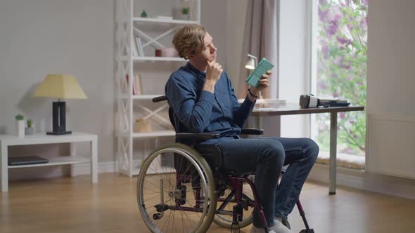 Wide Shot Thoughtful Man in Wheelchair Surfing Internet on Tablet Got an Idea