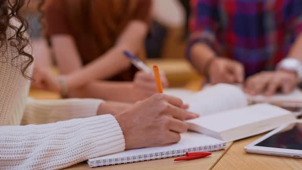 Two Teenage Female Friends Sitting at Table with Boy in Glasses and Shirt Writing Smiling Laughing